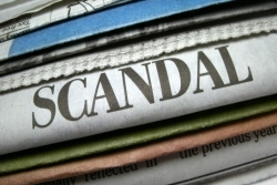 Stack of newspapers with one prominently proclaiming a scandal